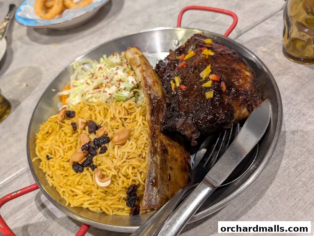 A platter of grilled ribs served with rice, salad, and nuts.