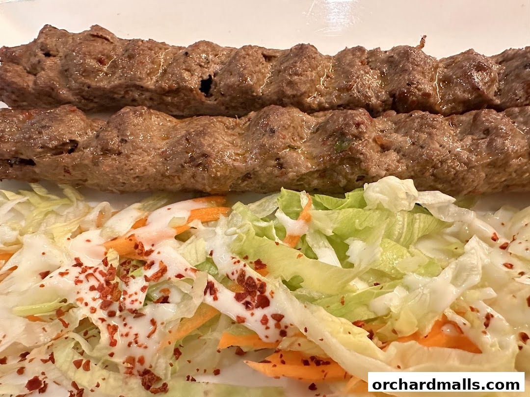 A close-up of two grilled kofta kebabs served with a fresh side salad.