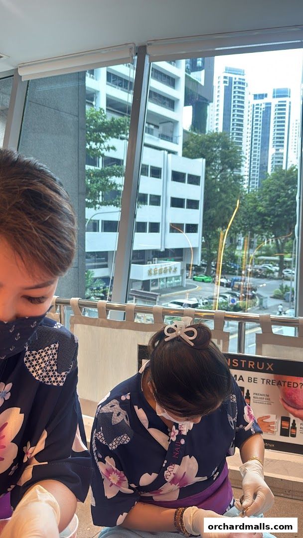 Nail technicians in uniform performing manicures with a city view.