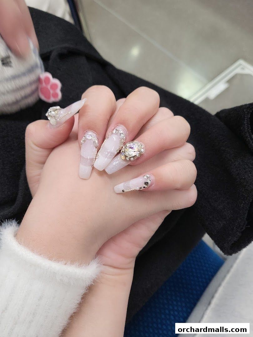 Close-up of hands with elaborate white and crystal-embellished long nails.
