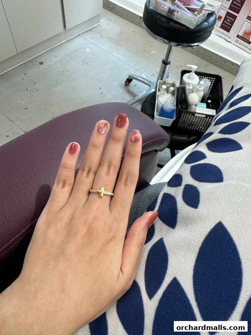 A close-up of a hand with freshly painted nails and a ring, resting on a chair.