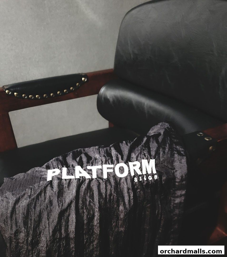 A black garment with the 'PLATFORM SALON' logo rests on a leather chair.