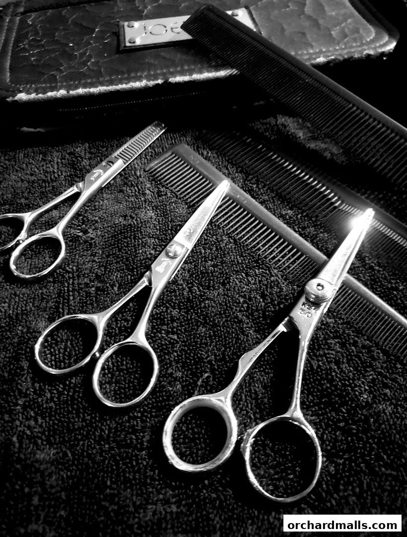 Close-up of professional hair cutting scissors and combs on a dark textured surface.