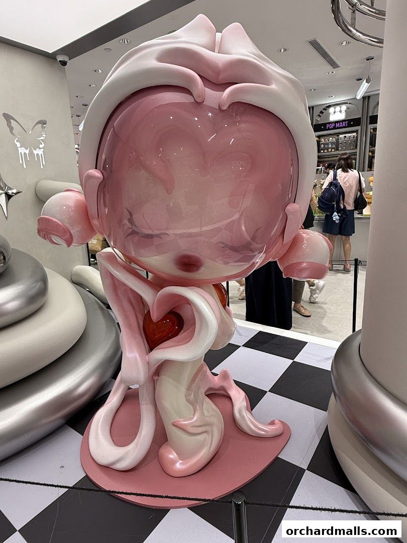 A large, pink, artistic figurine is displayed in a store with other shoppers in the background.