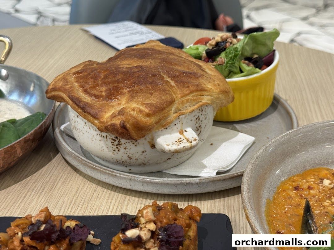 A close-up of a savory pie with a golden crust, served with a side salad and other dishes.