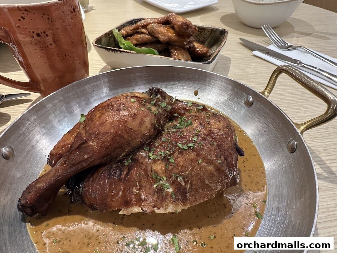 A close-up of a roasted chicken dish with a side of chicken wings and a mug.