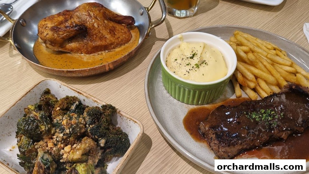 A table laden with delicious food, featuring roasted chicken, steak with fries, mashed potatoes, and roasted broccoli.