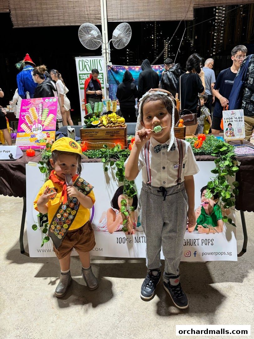 Two children enjoying popsicles at a Power Pops stall with a variety of fruit and popsicles displayed.