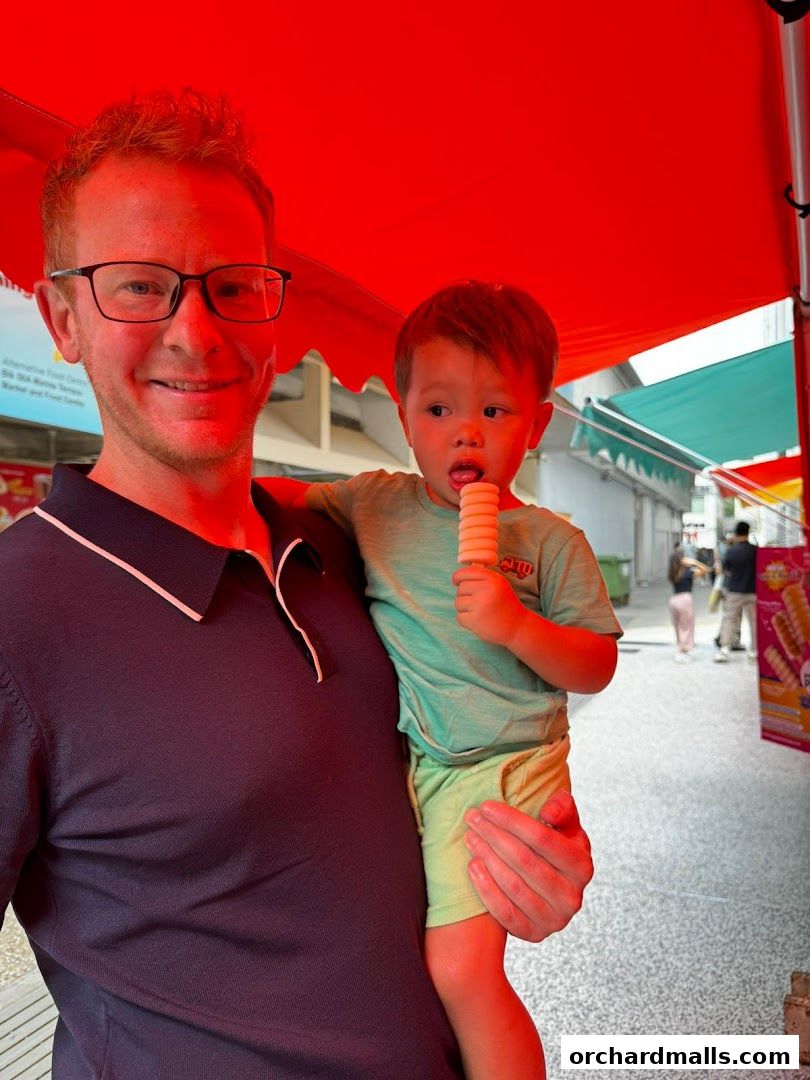 A man holds a child eating an ice cream cone under a red awning.