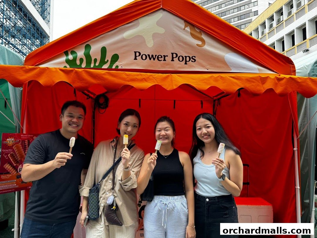 Four smiling people holding popsicles in front of a Power Pops stall.