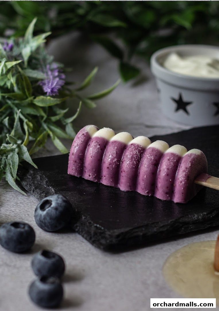 A blueberry and cream popsicle with fresh blueberries and greenery.