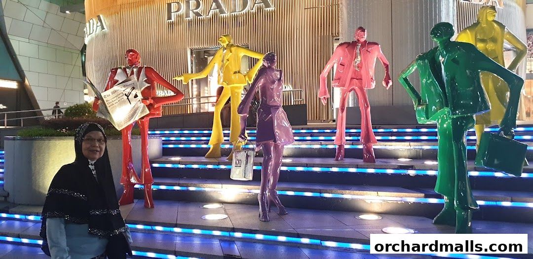 A woman poses in front of colorful mannequins outside a Prada store at night.
