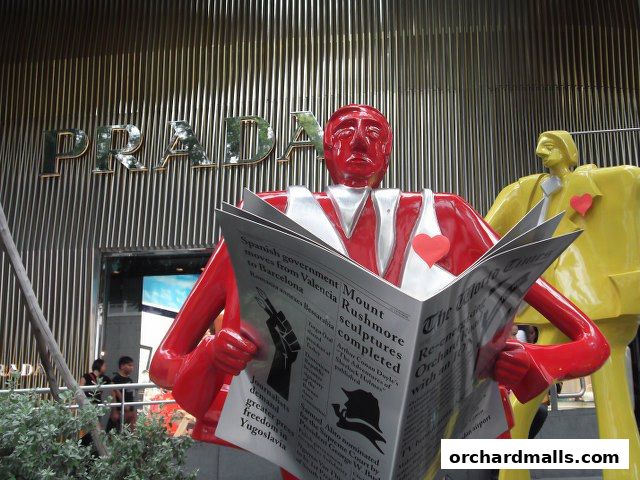 Prada storefront with artistic sculptures of figures reading newspapers.