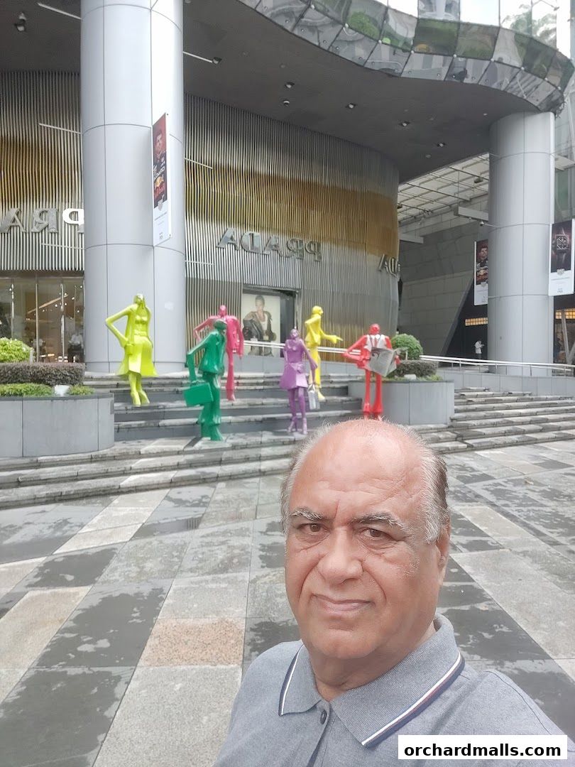 A man takes a selfie in front of the Prada Singapore Pte. Ltd. Office with colorful statues.