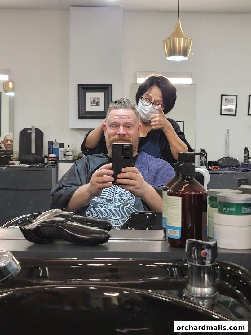 A barber gives a thumbs up while a customer takes a selfie during a haircut.