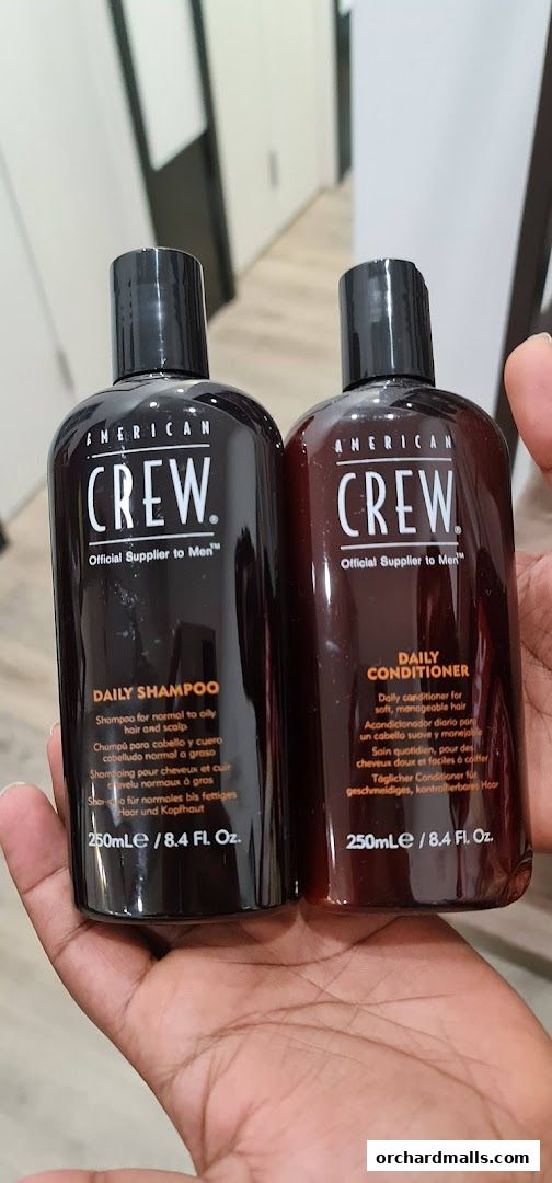 Two bottles of American Crew Daily Shampoo and Daily Conditioner held in a hand.