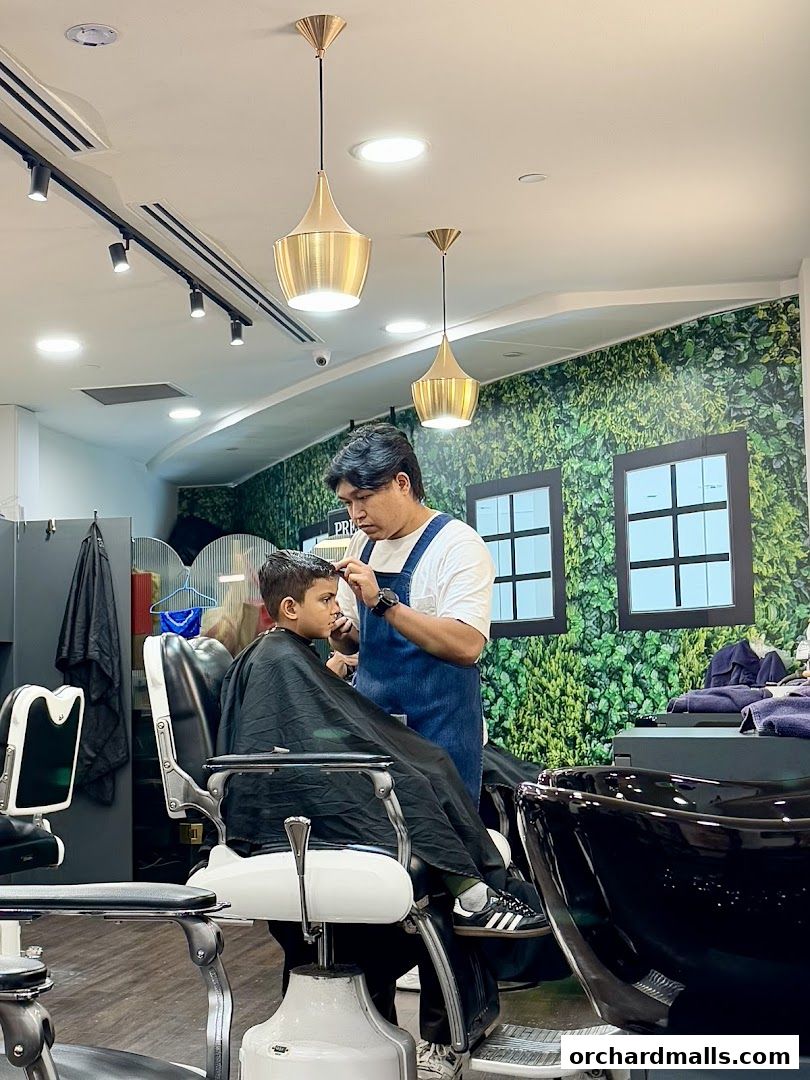 A barber cuts a young boy's hair in a modern, well-lit barbershop.