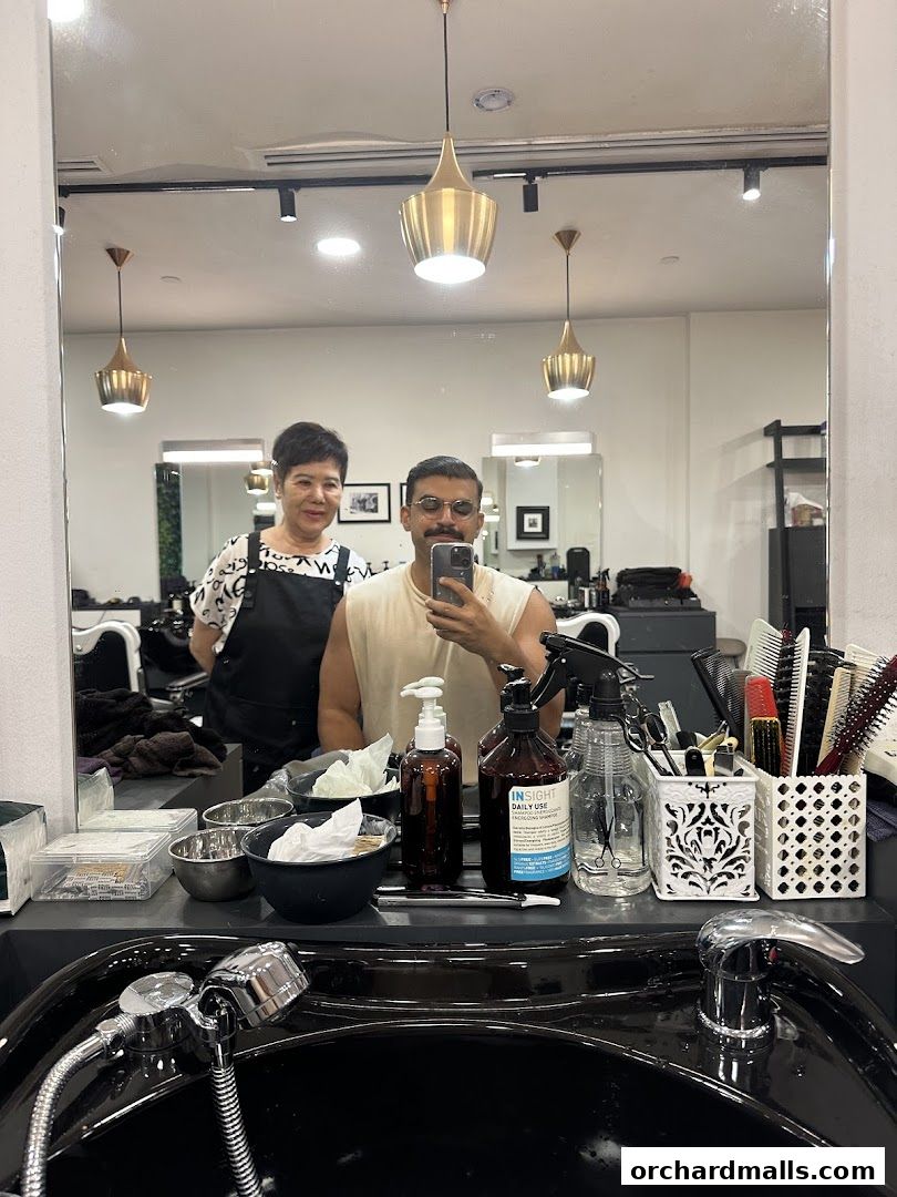 A man takes a selfie in a barber shop mirror with a barber behind him.