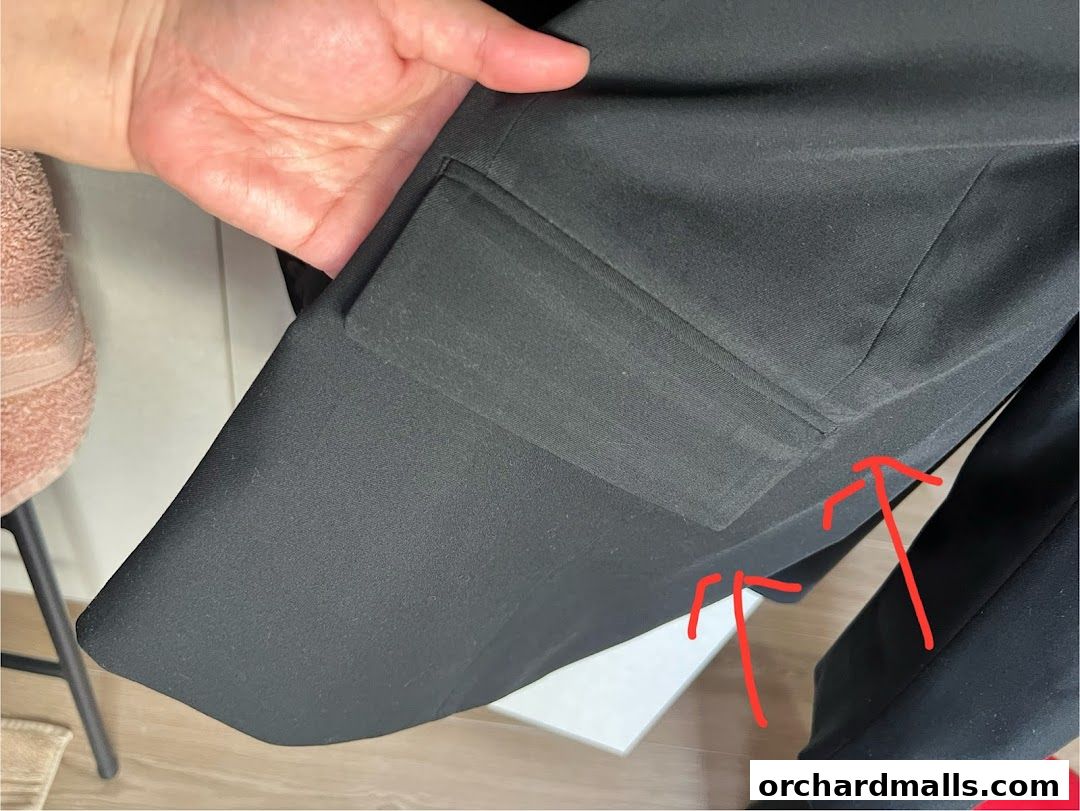 A hand holds a black garment, possibly a suit jacket, showing its lining and pockets.