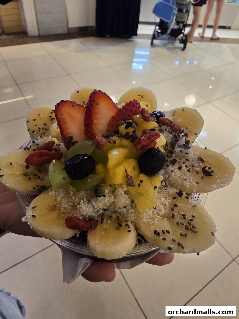 A hand holds a clear cup filled with a colorful acai bowl topped with fruits and seeds.
