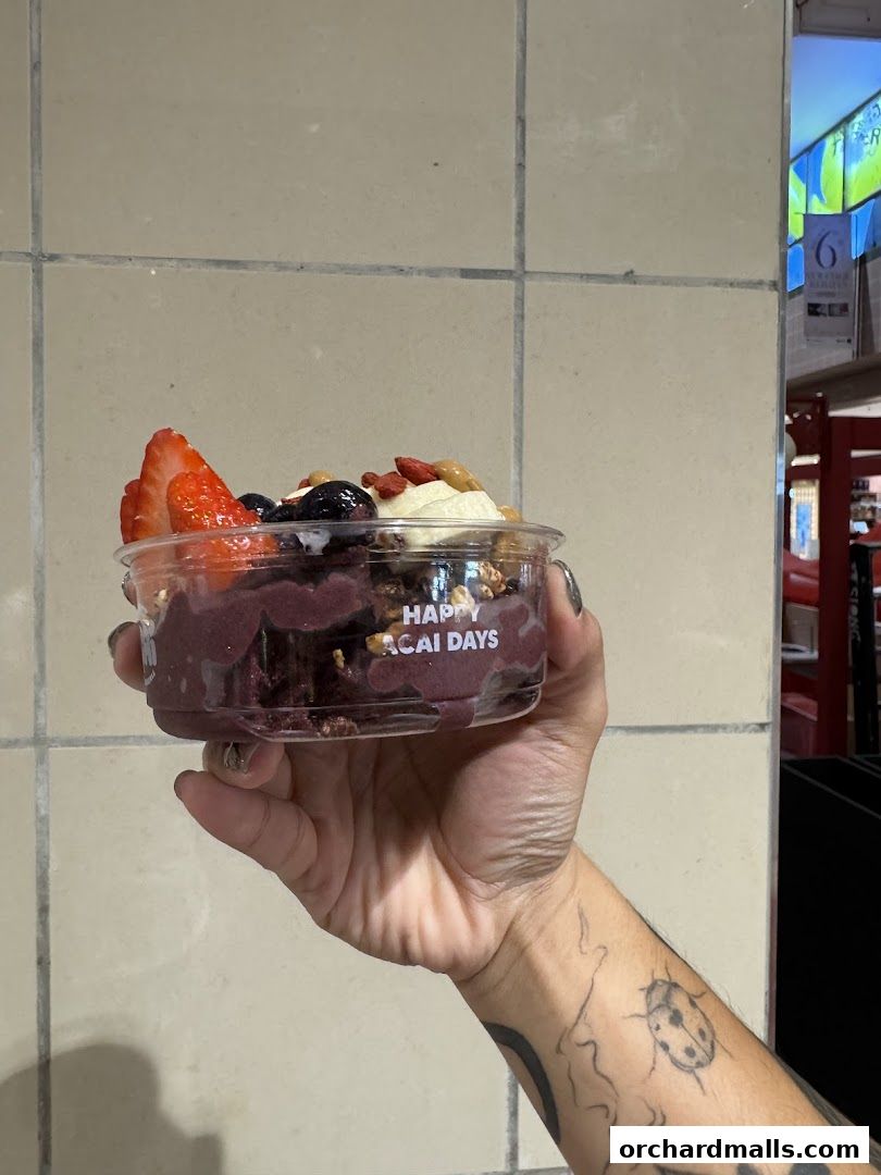 A hand holds a clear plastic cup filled with acai bowl topped with fruits and granola.