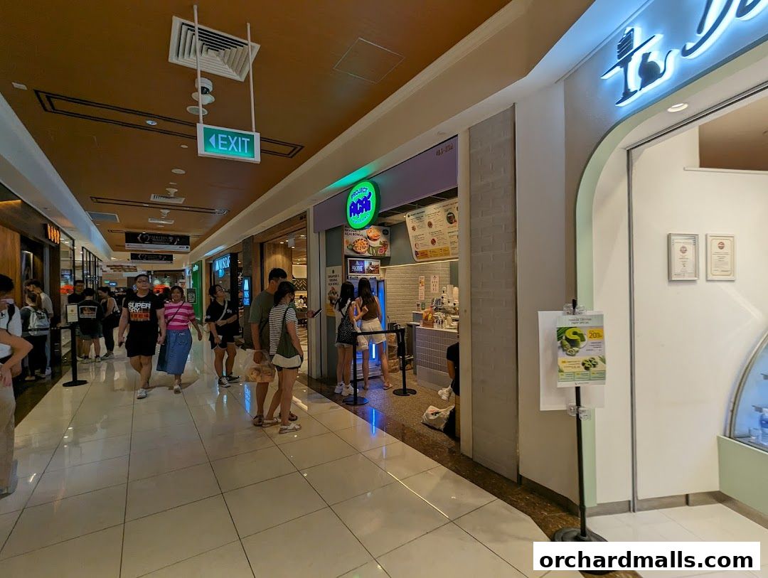People walk past Project Acai Ngee Ann City, a vibrant shop with a green logo and menu displayed.