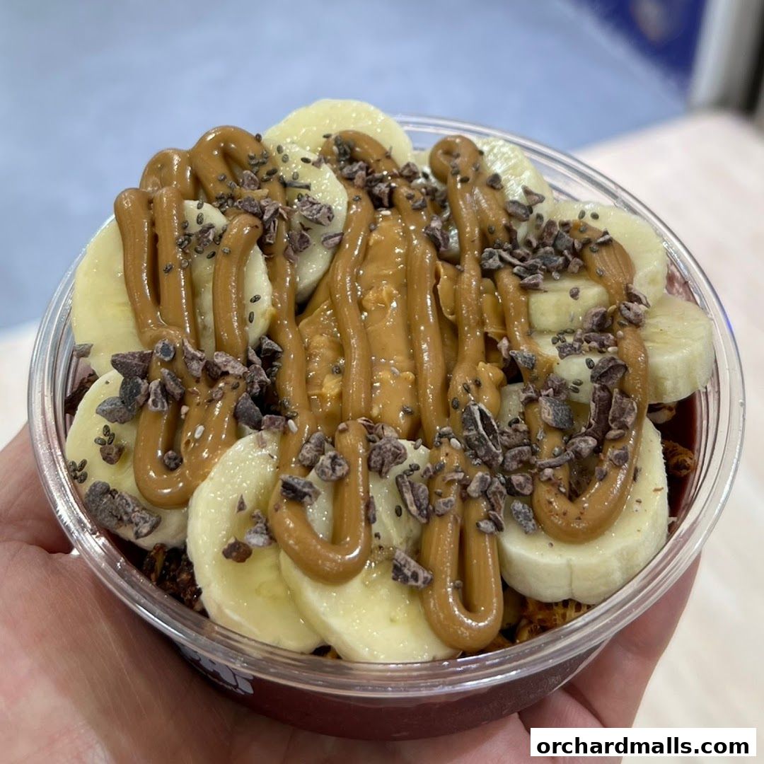 A close-up of an acai bowl topped with banana slices, peanut butter, and cacao nibs.