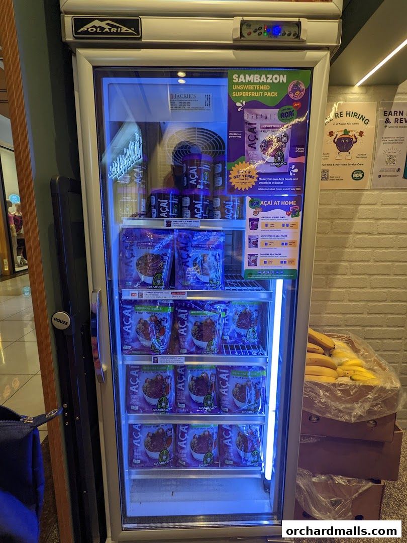 A refrigerated display case filled with frozen acai packs and a promotional poster.