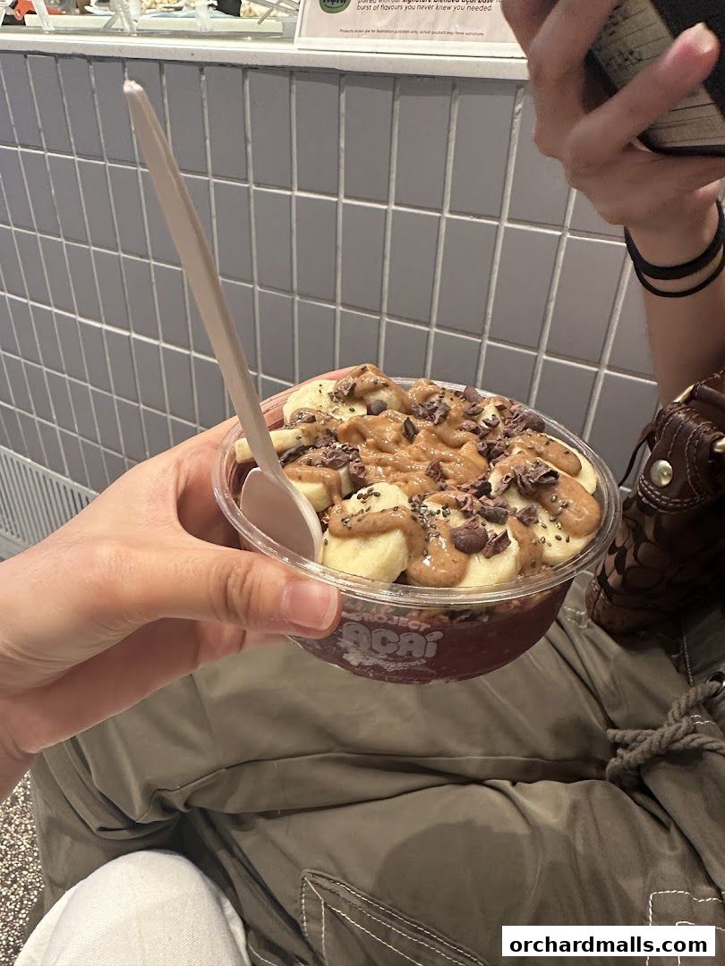 A hand holds a clear bowl of acai with bananas, nut butter, and chocolate chips.