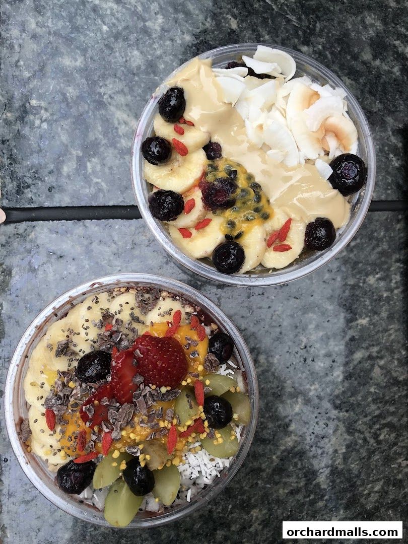 Two delicious acai bowls topped with fresh fruits, coconut, and seeds.