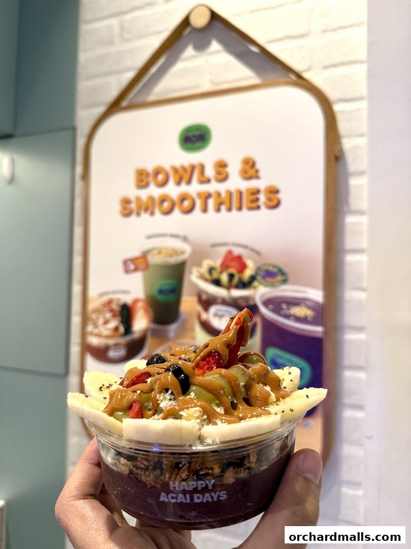 A hand holds a delicious acai bowl with fruits and granola in front of a menu board.