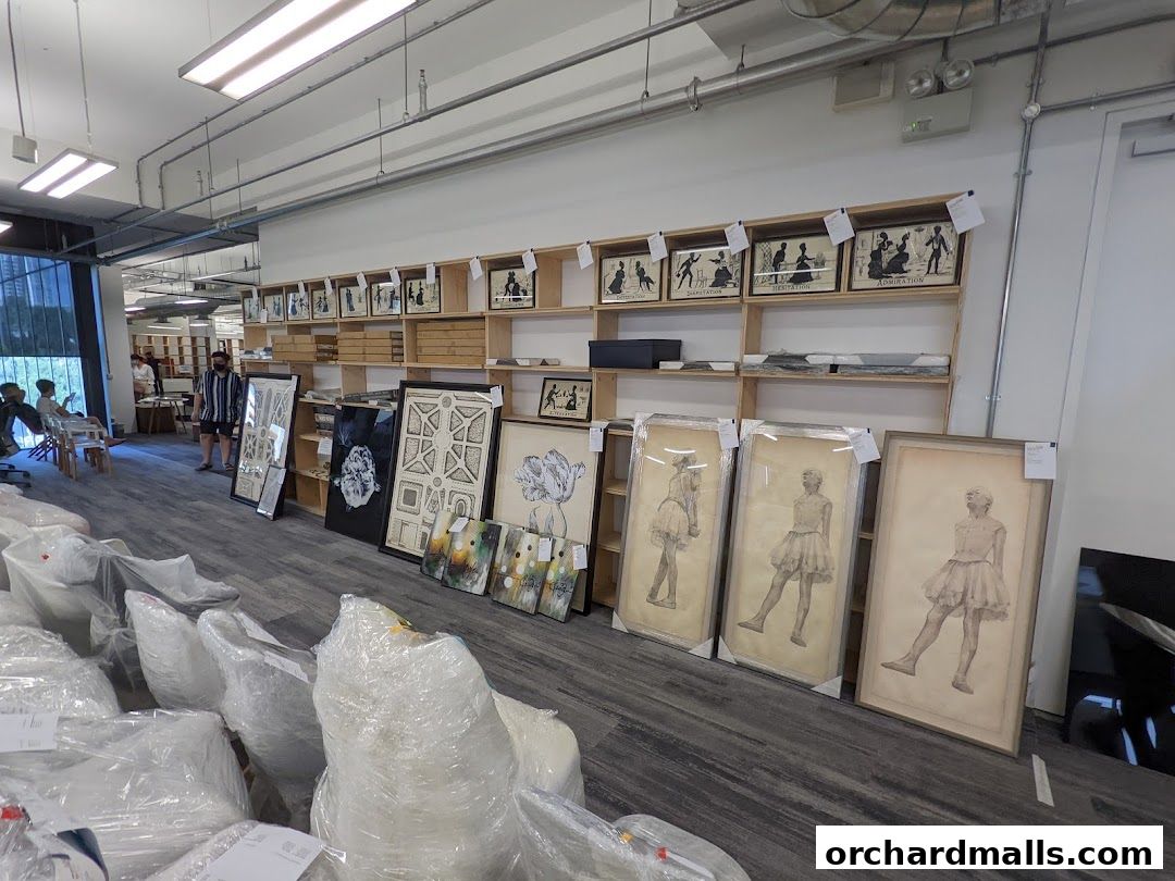 Interior view of a shop displaying framed artwork and art supplies on shelves and the floor.