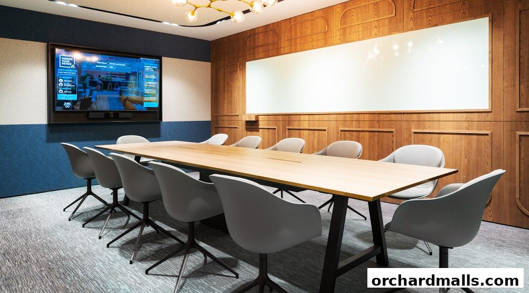 A modern conference room with a long wooden table, grey chairs, and a large screen.