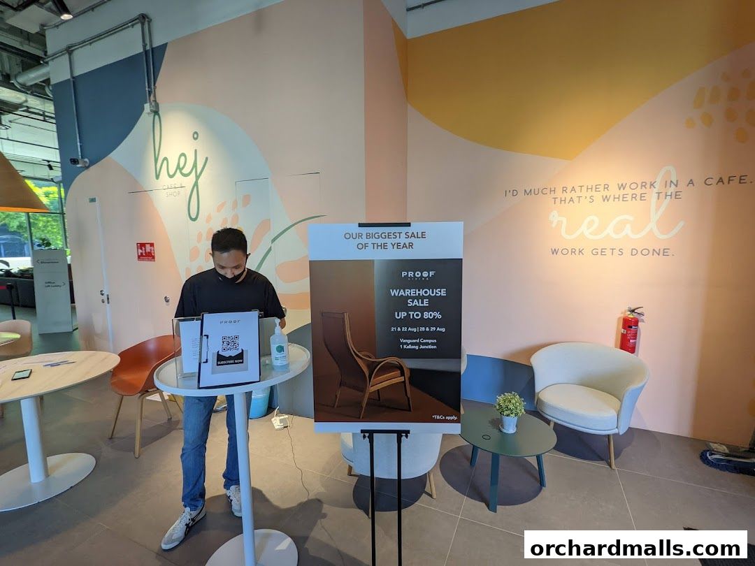A man stands near a display for a warehouse sale at Proof, with cafe-themed decor on the wall.