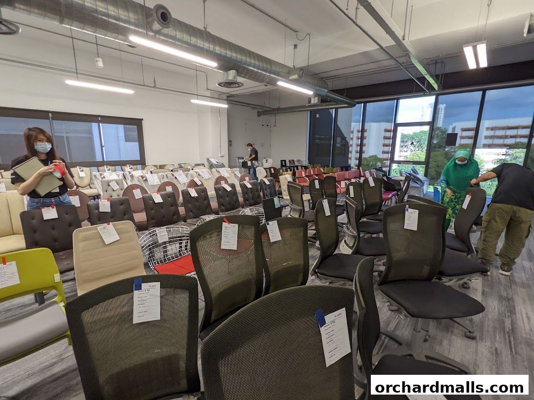 A wide selection of office chairs are displayed in a brightly lit showroom with people browsing.