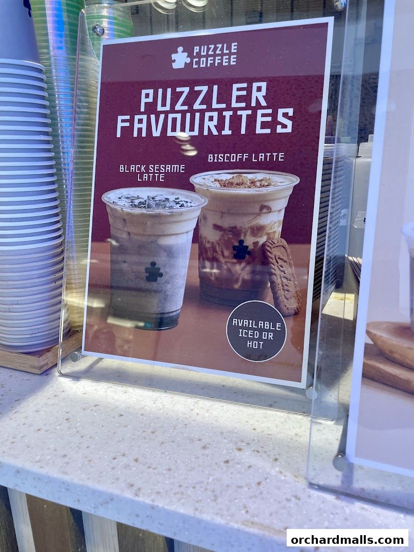 A sign showcasing Puzzle Coffee's 'Puzzler Favourites' including Black Sesame Latte and Biscoff Latte.