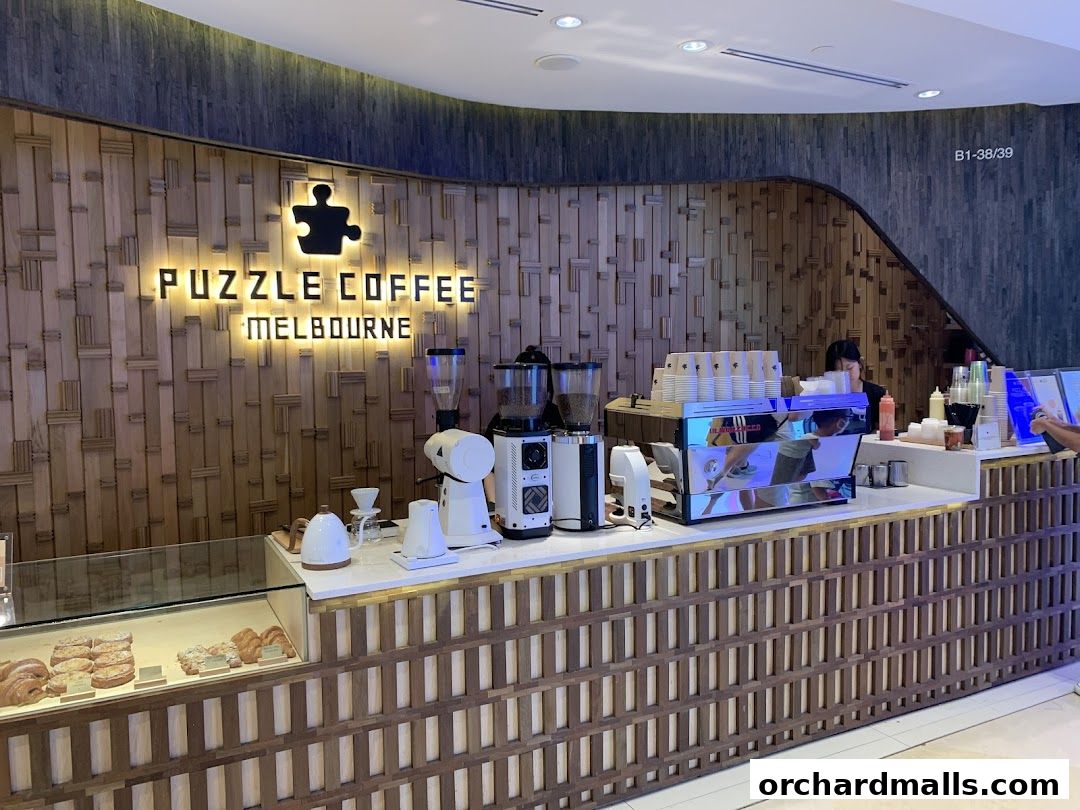 The interior of Puzzle Coffee Melbourne, featuring a modern wooden counter with coffee machines and pastries.