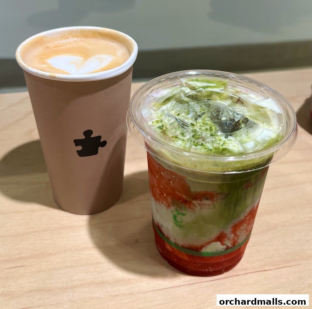 Two refreshing drinks, one with latte art and the other a layered matcha beverage, sit on a wooden surface.
