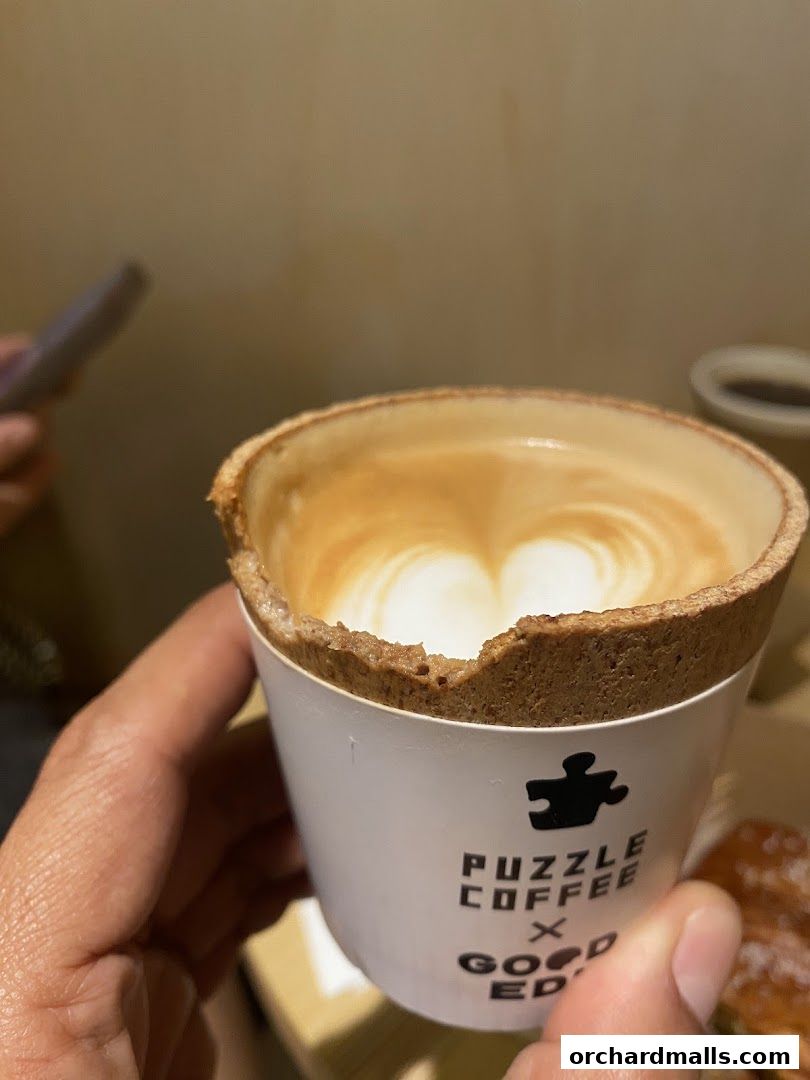A hand holds a coffee cup with latte art and a cookie rim, branded Puzzle Coffee.