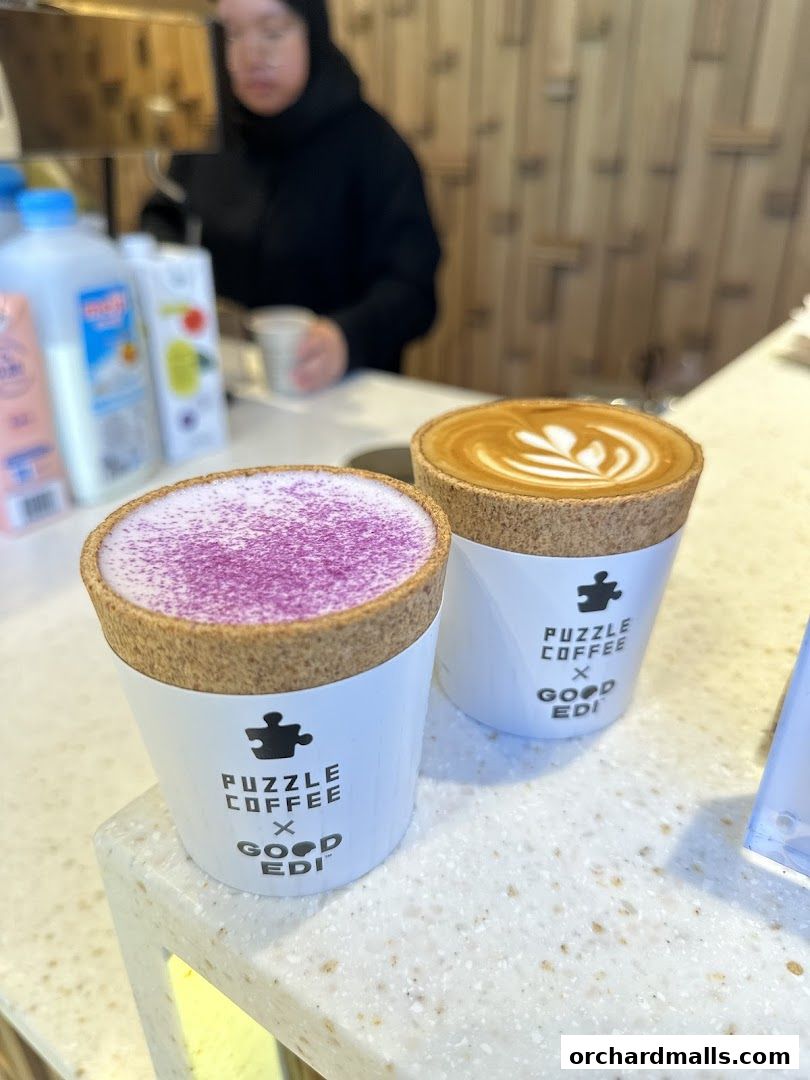 Two beautifully crafted coffee drinks, one with purple topping and the other with latte art, sit on a counter.