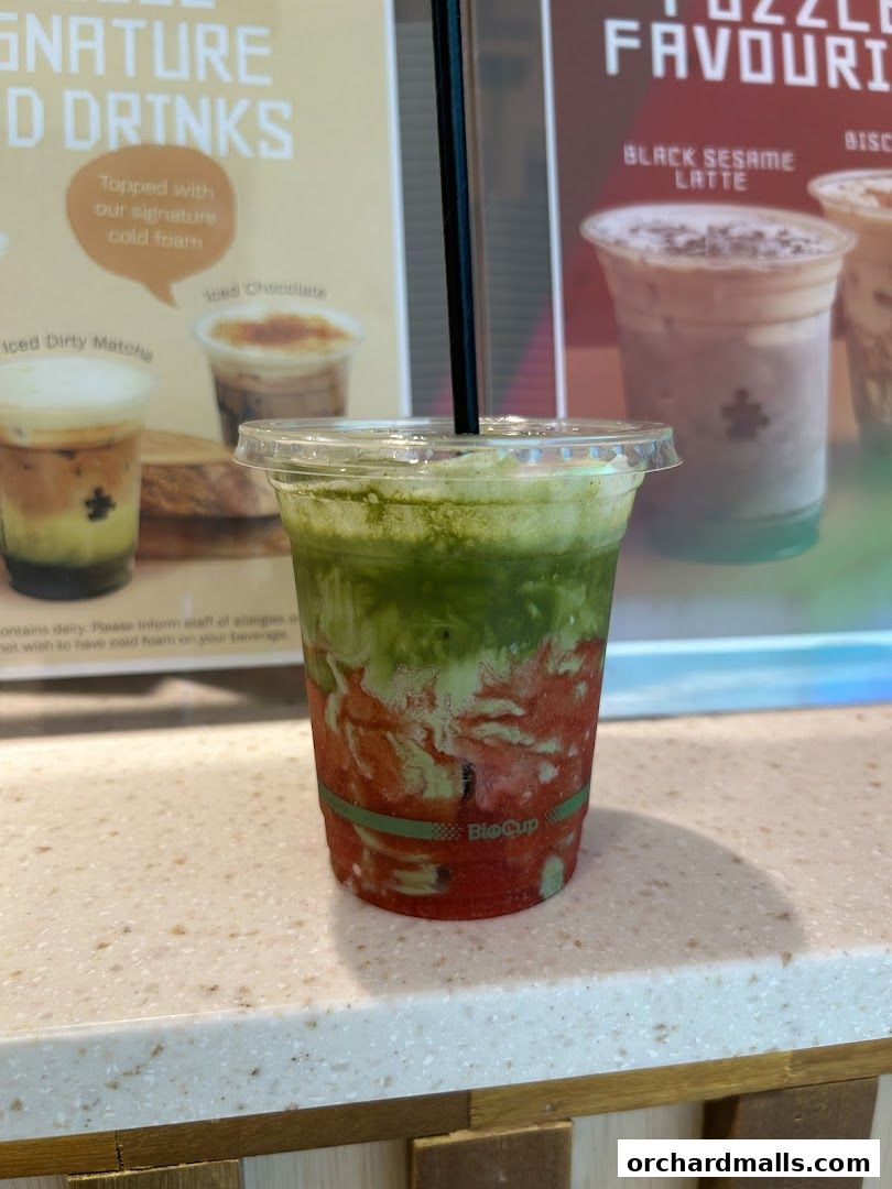 A close-up of a layered green and red drink with a straw in a clear cup.