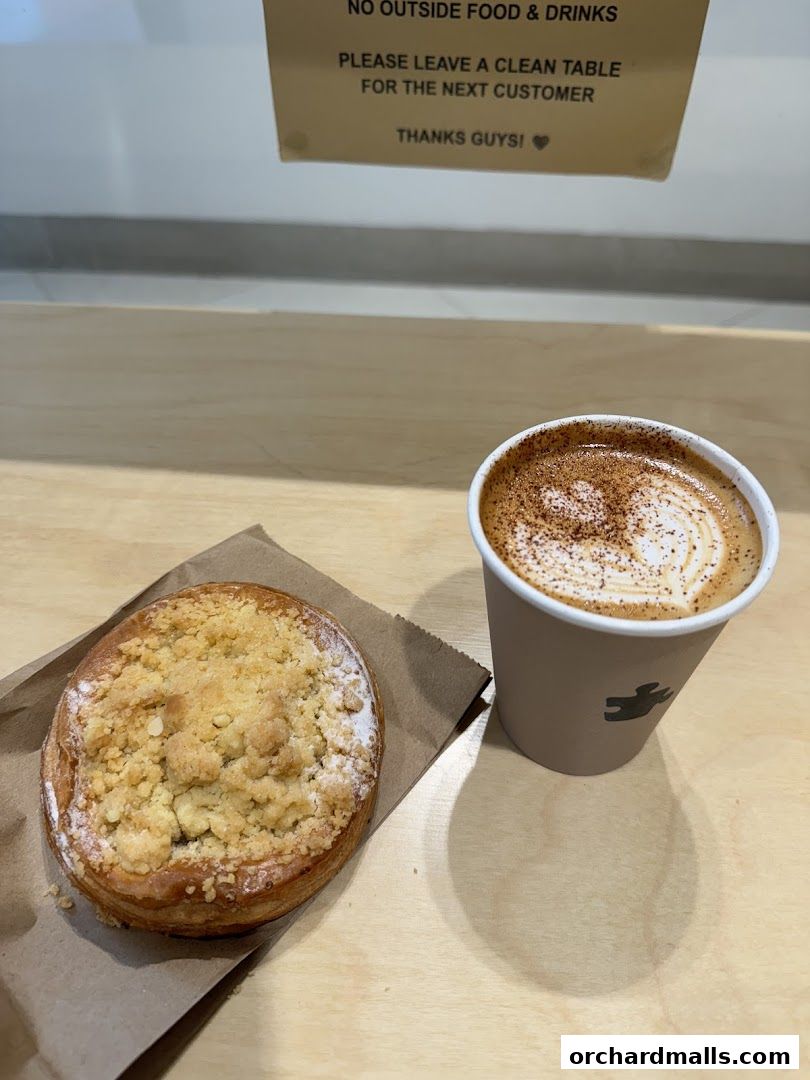 A coffee with latte art and a pastry sit on a wooden table.