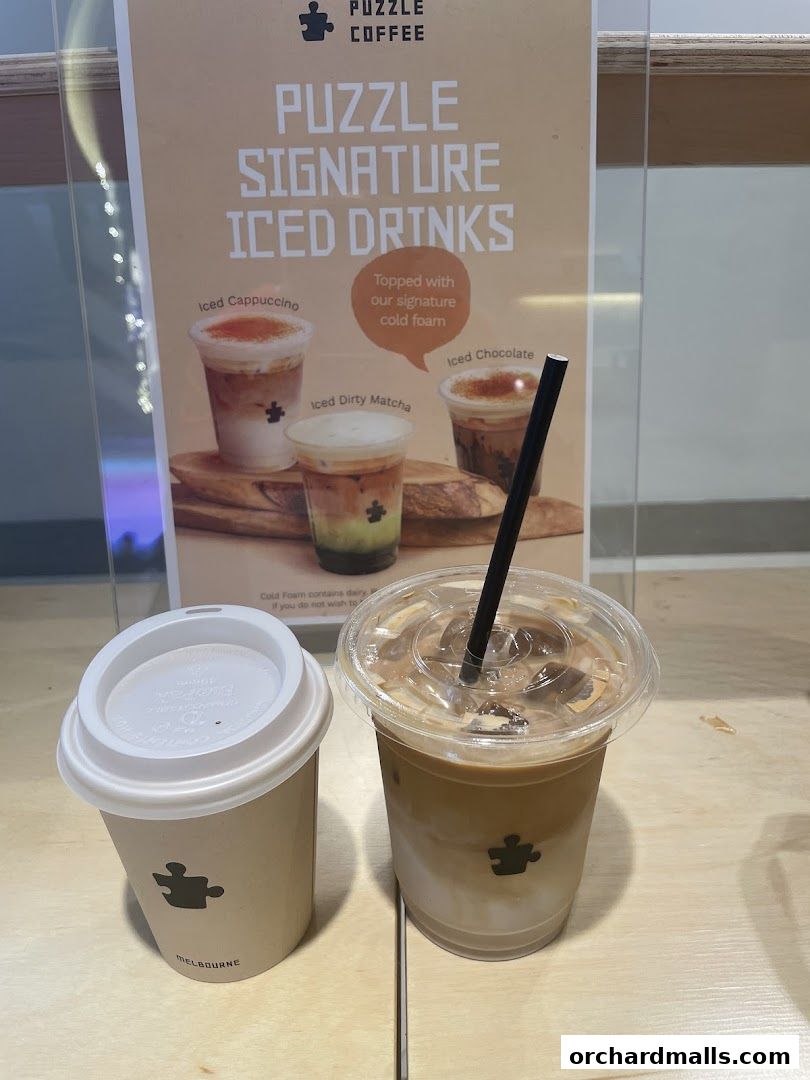Two coffee drinks from Puzzle Coffee, one in a paper cup and another in a plastic cup with a straw.