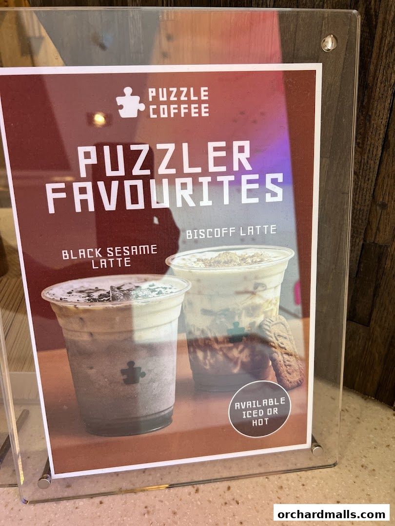 A sign showcasing Puzzle Coffee's popular Black Sesame Latte and Biscoff Latte.