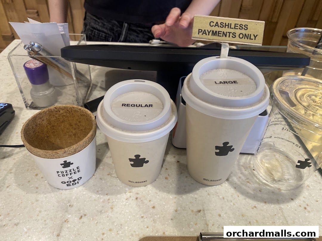 Two coffee cups labeled 'Regular' and 'Large' from Puzzle Coffee, with a cashless payment sign.