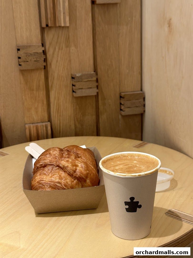 A freshly baked croissant and a cup of coffee with latte art on a wooden table.