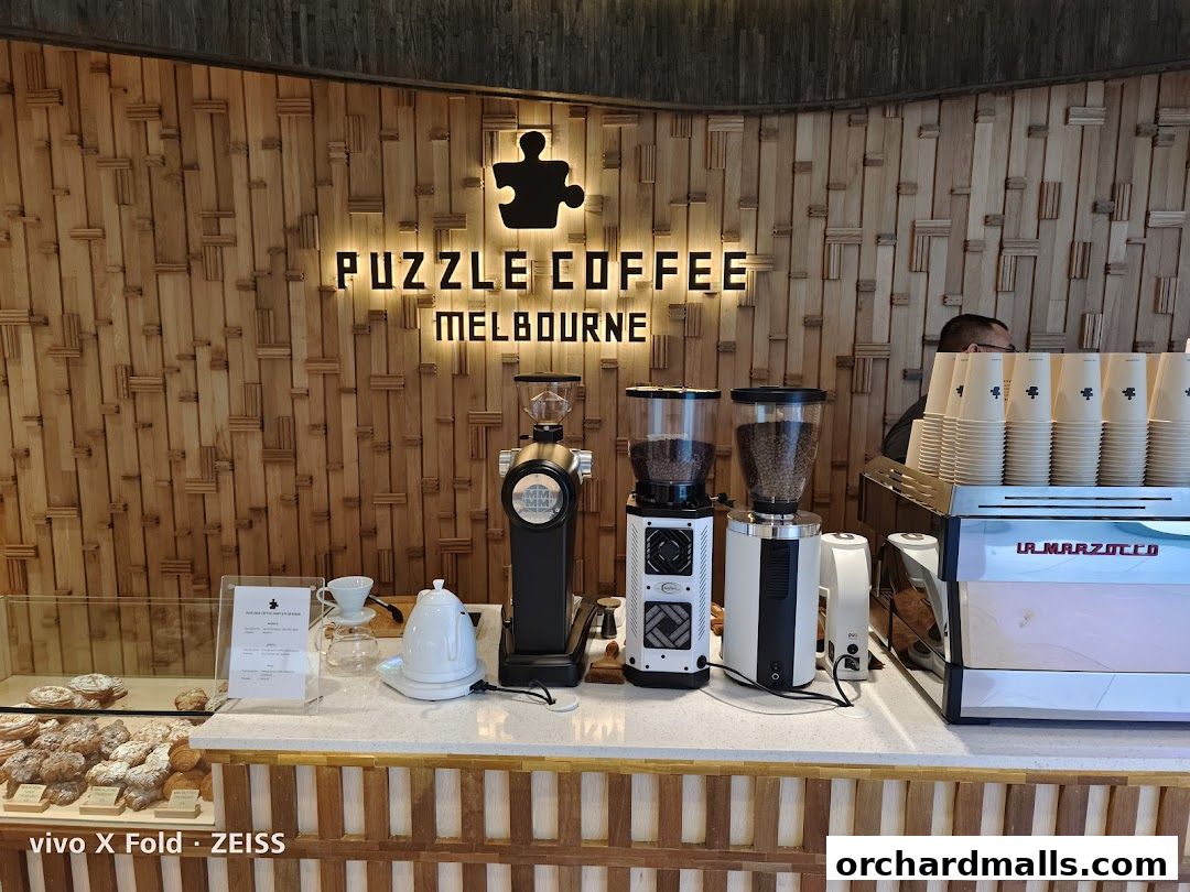 A coffee counter with grinders, espresso machine, cups, and pastries at Puzzle Coffee Melbourne.