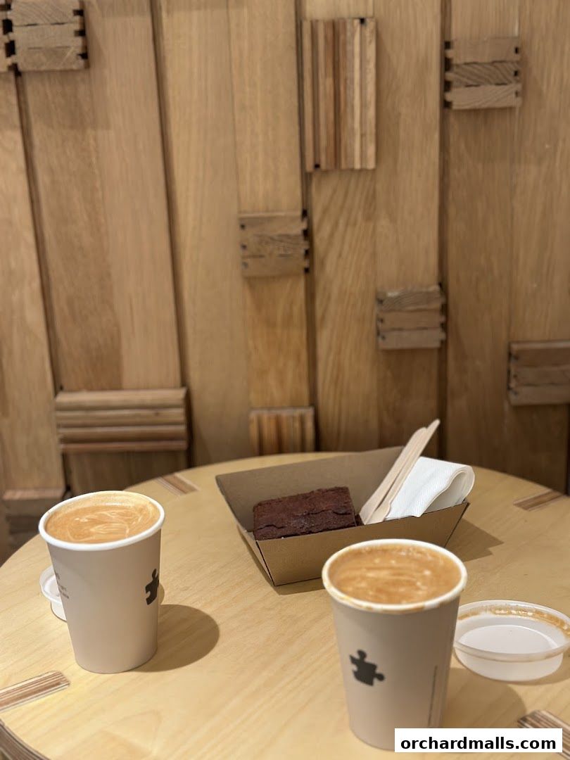 Two cups of coffee and a brownie are on a wooden table in a cafe.