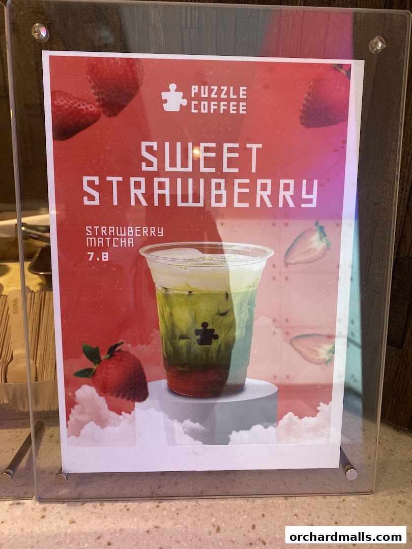 A sign for Puzzle Coffee featuring a strawberry matcha drink with strawberries and clouds.