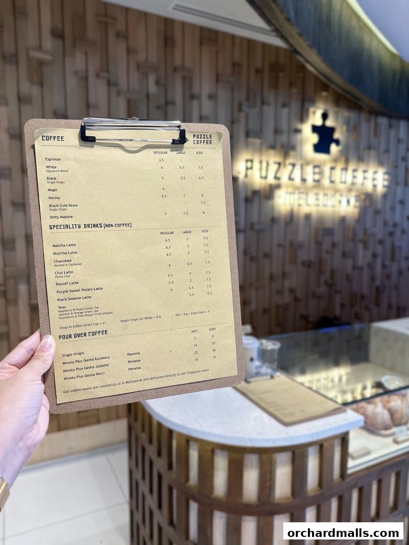 A hand holds a coffee menu from Puzzle Coffee, with the shop's interior visible in the background.